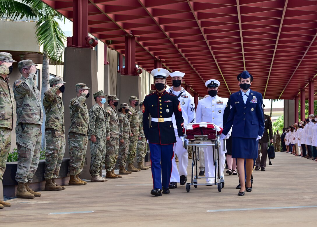 Service members walk with a flag-draped casket as fellow troops salute.