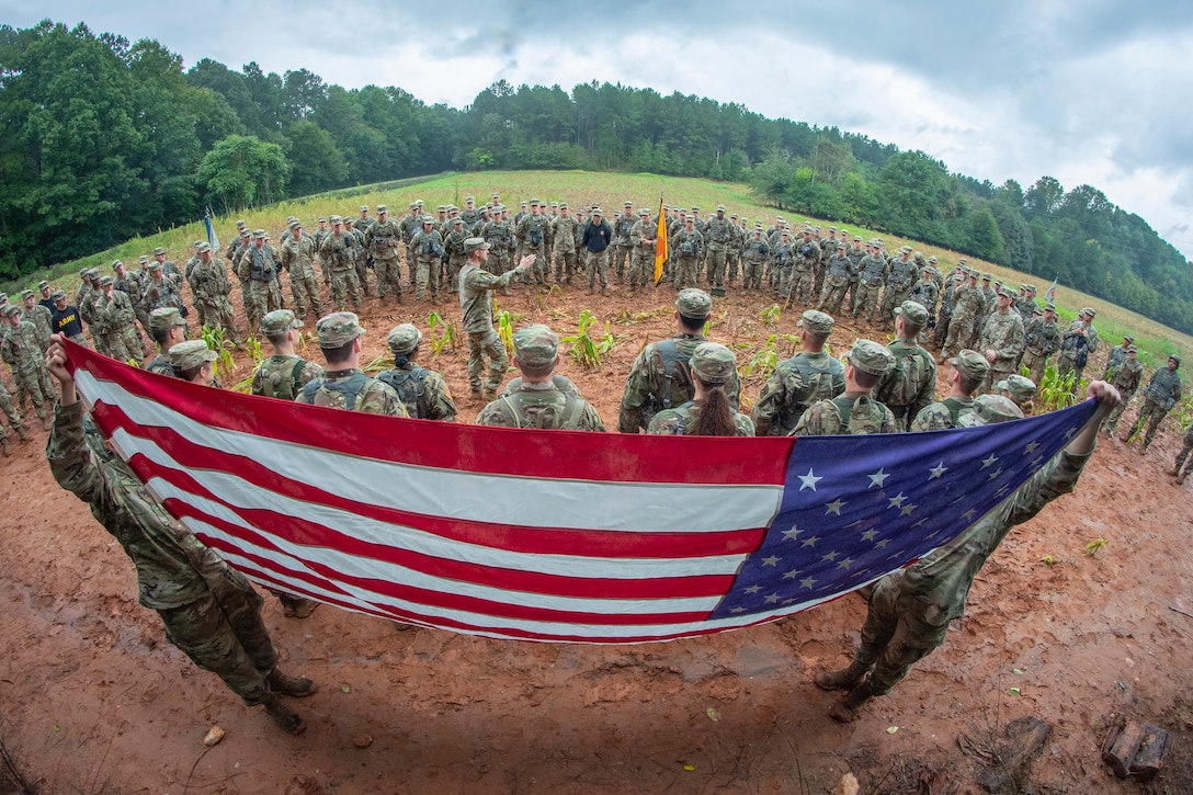A group of cadets stand in a large field with two of them holding up the American flag.