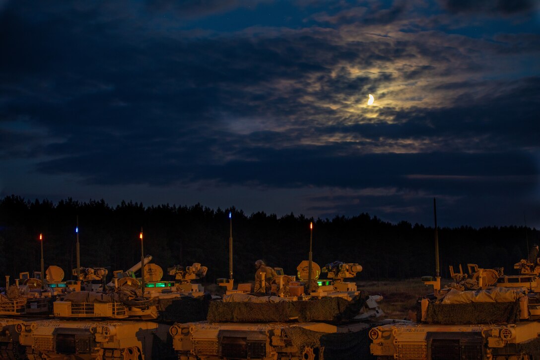 A line of tanks sit under a dark, moonlit sky.