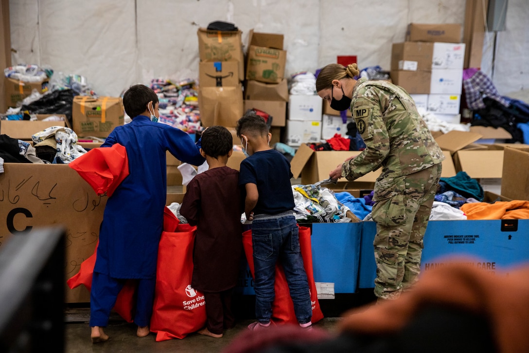 A soldier helps three Afghan children look for clothes at a donation center.