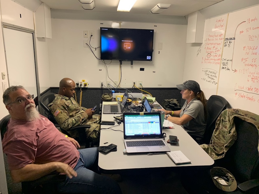 three people sit around a table in a mobile command center