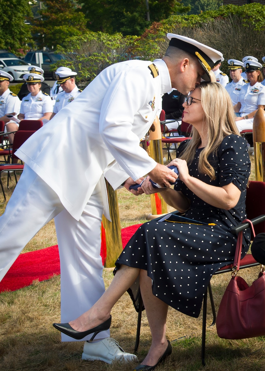 210924-N-WJ362-0098 EVERETT, Wash. (September 24, 2021) Capt. Jonas C. Jones, outgoing Commander, Navy Region Northwest Reserve Component Command (NRNW RCC) Everett, hands the ceremonial flag to his wife during NRNW RCC Everett’s change of command on board Naval Station Everett, Wash. (U.S. Navy photo by Mass Communication Specialist 1st Class Kleynia R. McKnight)