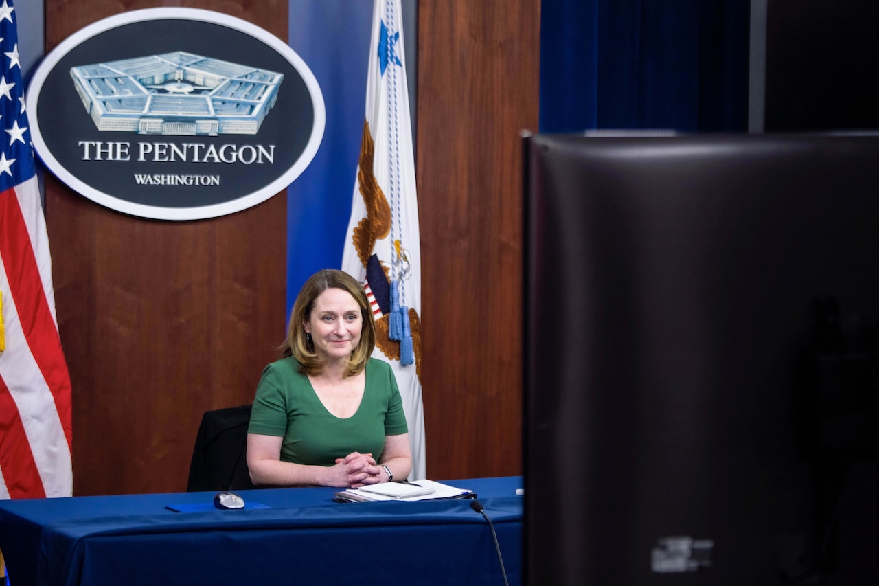 The deputy defense secretary sits at a table and speaks toward a screen.