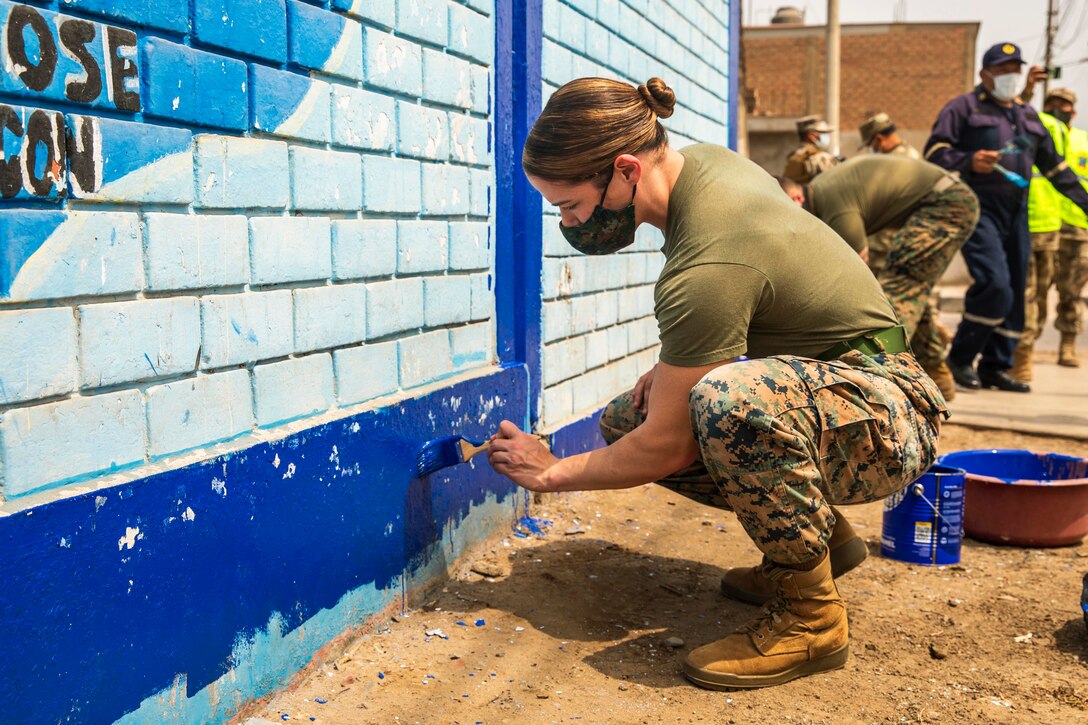 A Marine paints a wall with fellow service members.