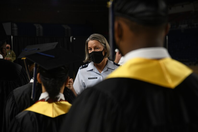 A female airman looks toward three people in graduation garb.