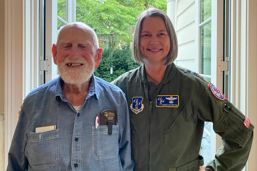 An older man and a woman in a pilot uniform stand beside each other.