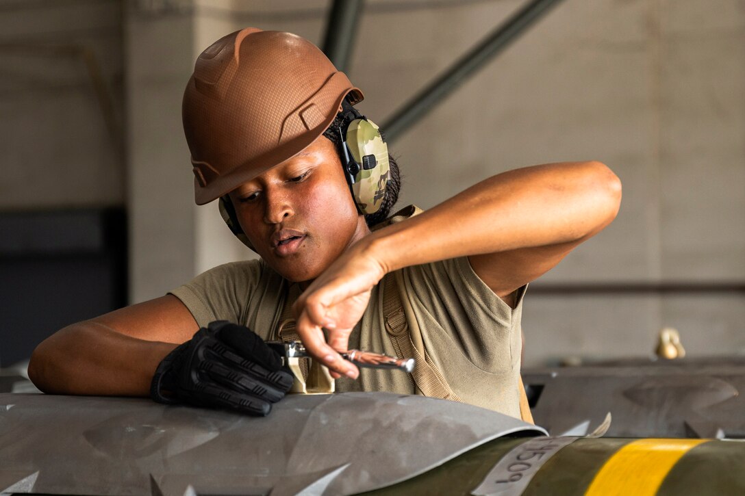 An airman wearing protective gear performs maintenance in a garage-like area.
