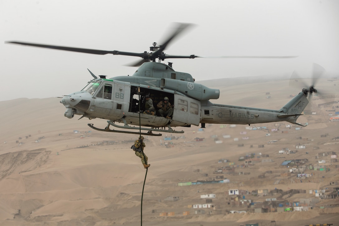 A Marine fast-ropes down a rope attached to an airborne helicopter.