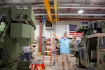 A man in a warehouse points at two separate vehicles with built-in rocket launchers.