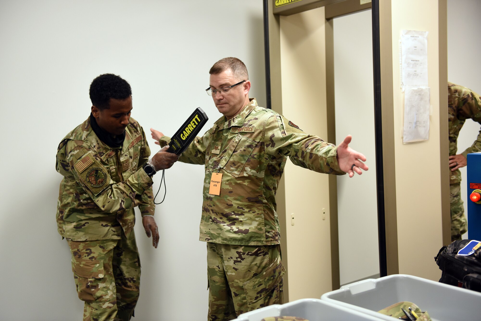 Photo shows Airman using a metal detector wand on another Airman.