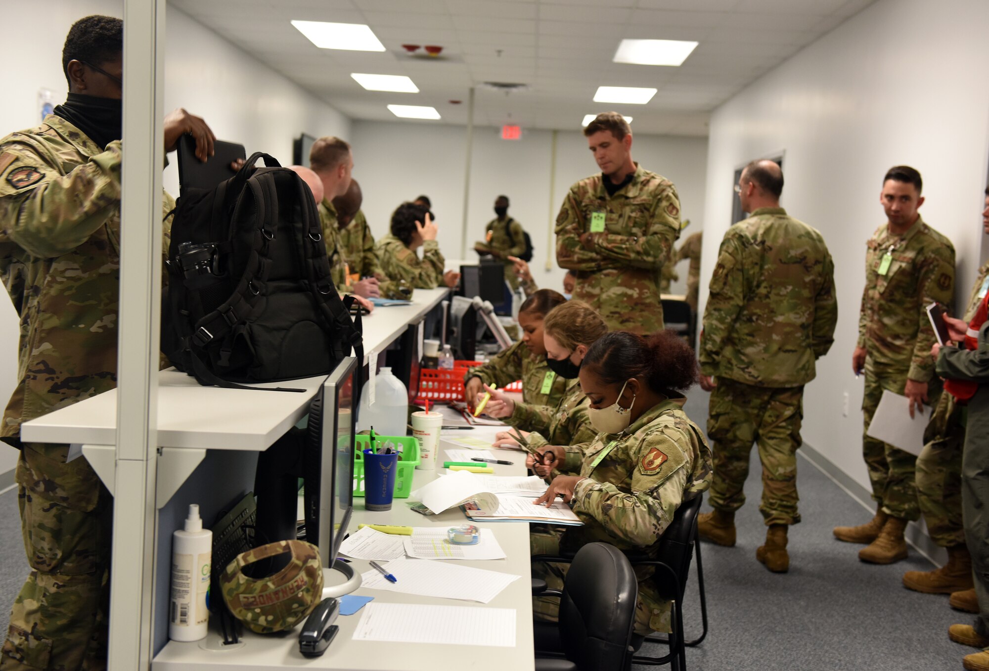 Photo shows Airmen walking by alongside a counter with personnel behind it.