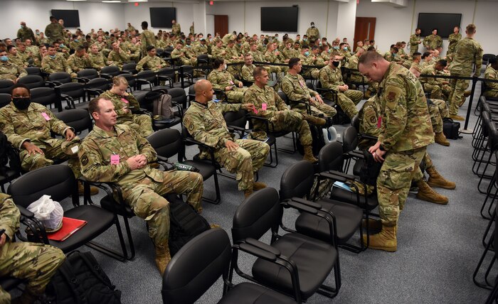 Photo shows group of Airmen sitting in large room with chairs.
