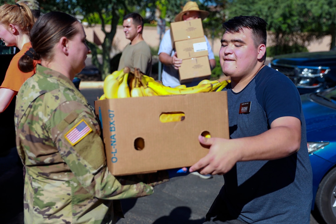 A female army soldier gives a box of groceries to a male civilian.