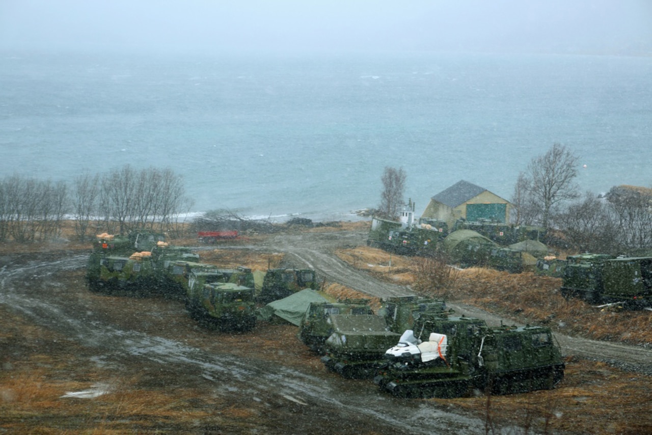 Military vehicles are parked in a muddy area along a coastline.
