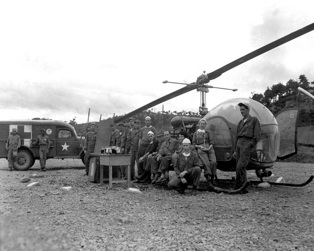 People pose for a photo in front of a helicopter.