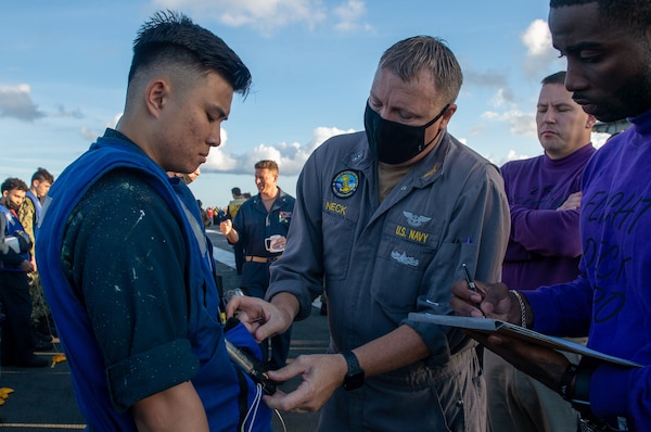 Chief Warrant Officer 4 Michael Neck, center, an inspector assigned to the Board of Inspection and Survey (INSURV), checks a CO2 cylinder on a life preserver on the flight deck of the Nimitz-class aircraft carrier USS Harry S. Truman (CVN 75).