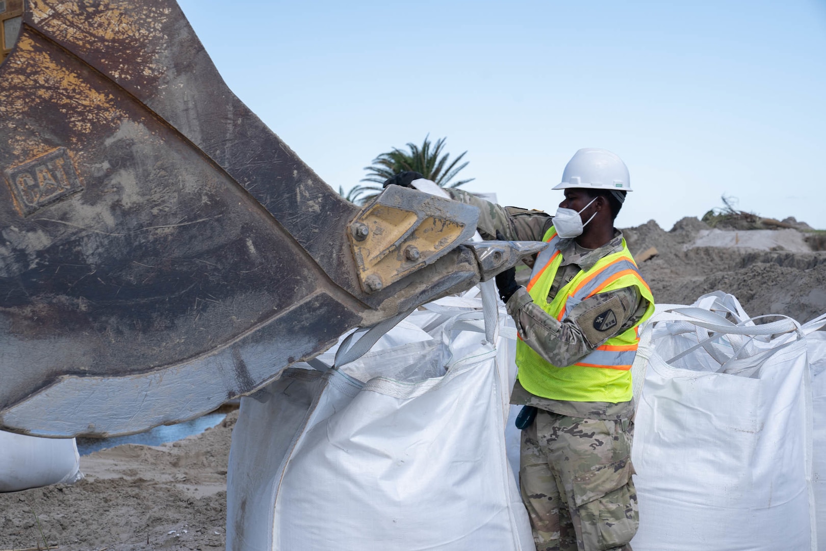 A Louisiana National Guardsman assigned to the 225th Engineer Brigade hooks a 3-by-3 foot sack filled with up to 4,000 pounds of sand to an excavator bucket to temporarily repair levee breaches in Grand Isle, Louisiana, Sept 24, 2021. The 225th has emplaced more than 1,100 sacks of sand along the coastline levees in Grand Isle.