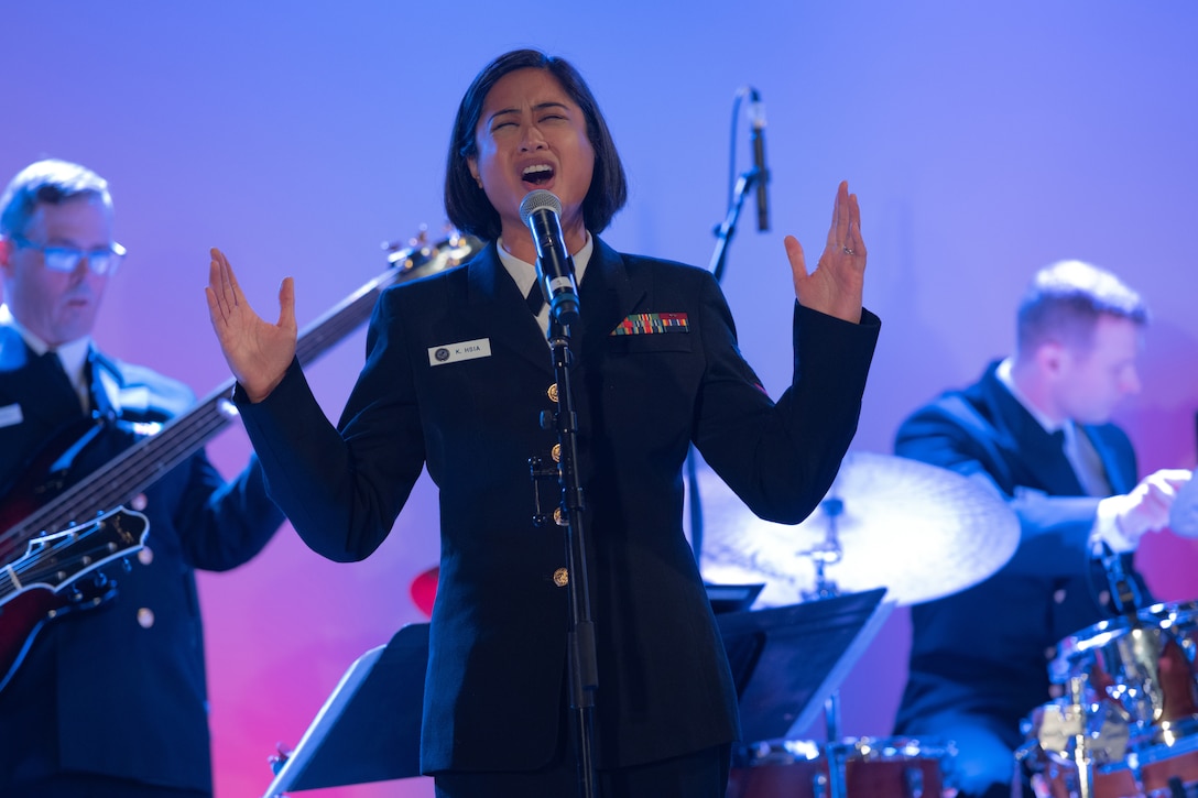 A sailor sings while others play instruments behind her.