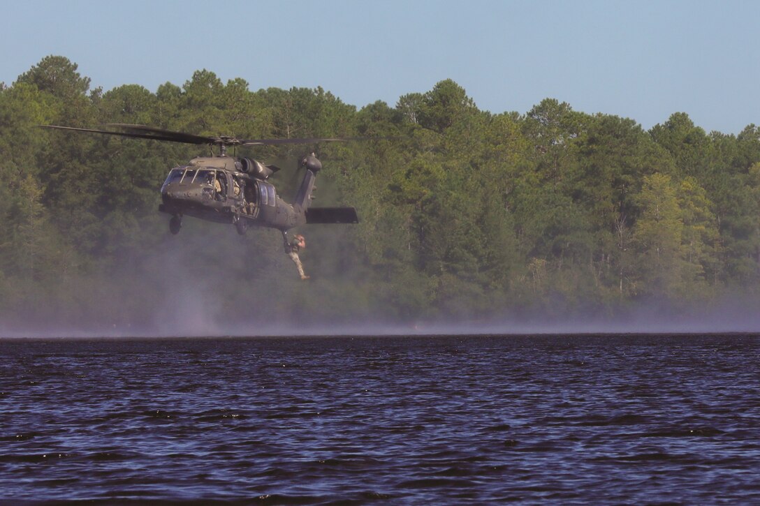 A soldier jumps out of a helicopter hovering above a lake.