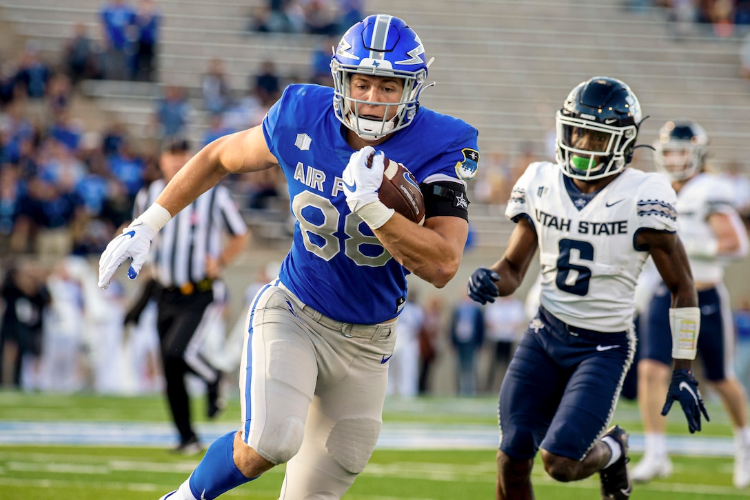 An Air Force football player runs with the ball as the opposite team trails behind.