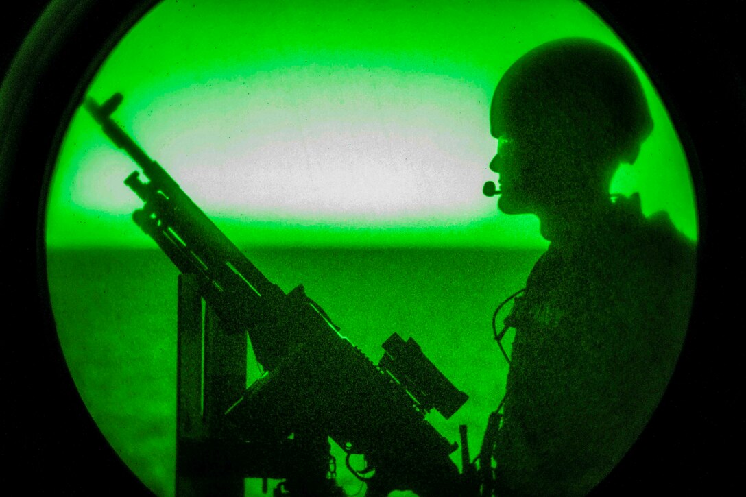 A sailor illuminated by green light stands near a weapon.