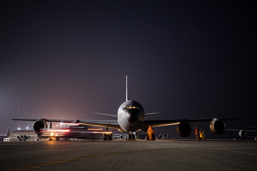 An Air Force Stratotanker aircraft sits on a dark flight line with personnel nearby.