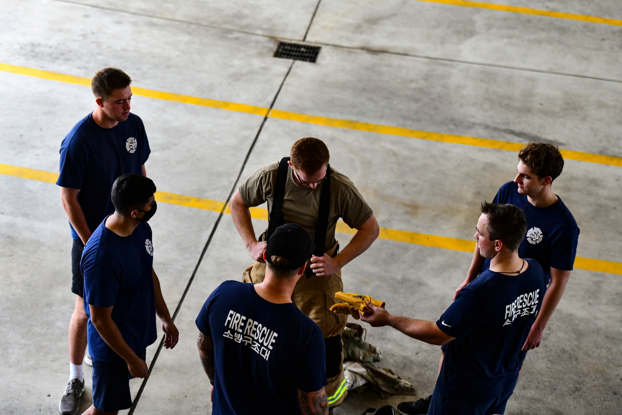 Firefighters teach an Airmen how to wear a firefighter suit.