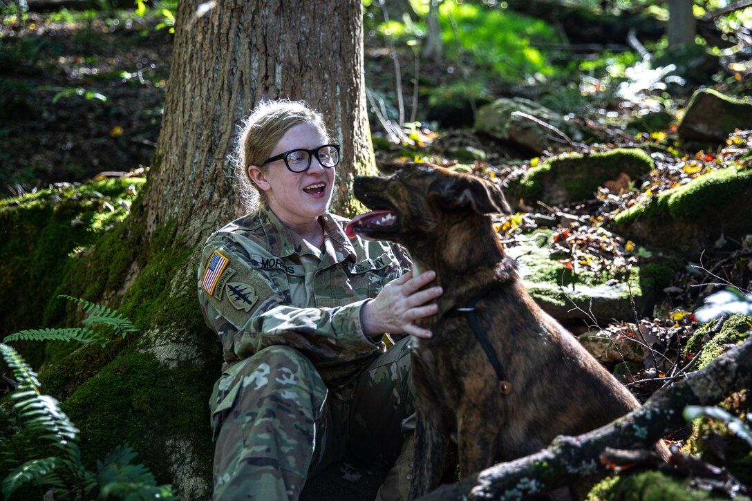 A soldier laughs as she plays with a dog.