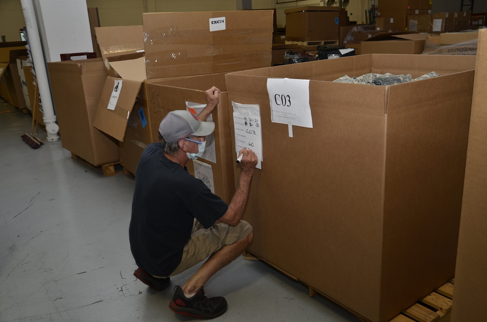 Crouched man writes on a box label