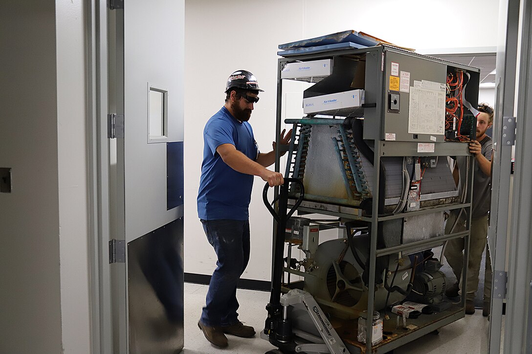 IMAGE: NAVFAC Heating, Ventilation and Air Conditioning technicians remove an old Computer Room Air Conditioning unit from a workspace in Hopper Hall—NSWCDD DNA’s main building in Virginia Beach, Va. To date, the DNA Facilities Team has replaced six of the oldest units in Hopper Hall with new units that better control humidity, especially during warmer seasons.