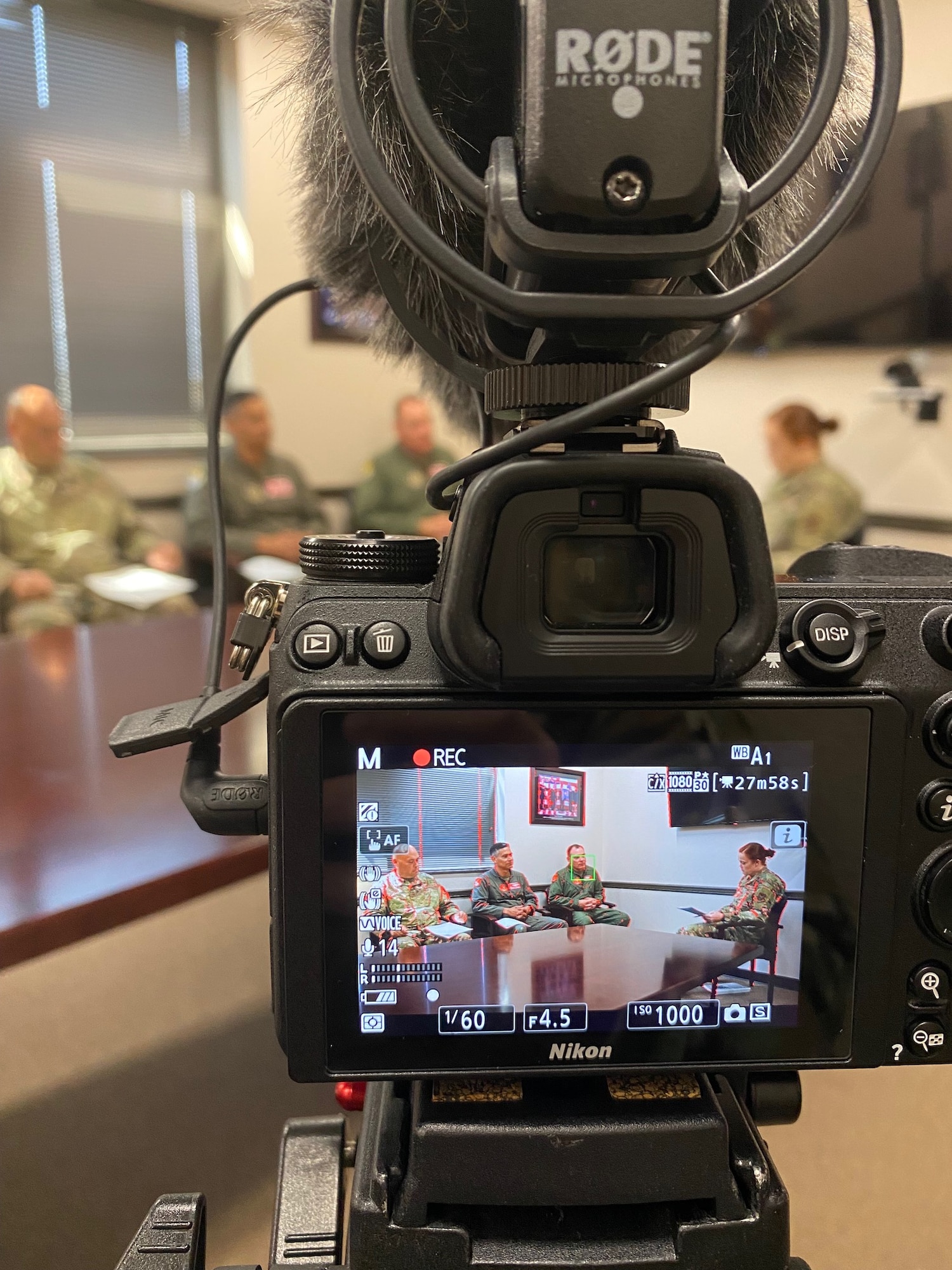 Four airmen are sitting in chairs facing each other behind a camera screen.