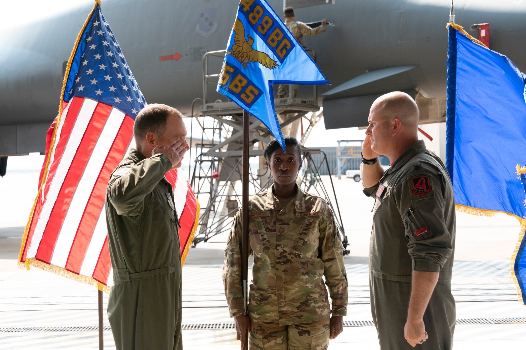 Two Airmen salute each other while a third stands at attention holding a flag.