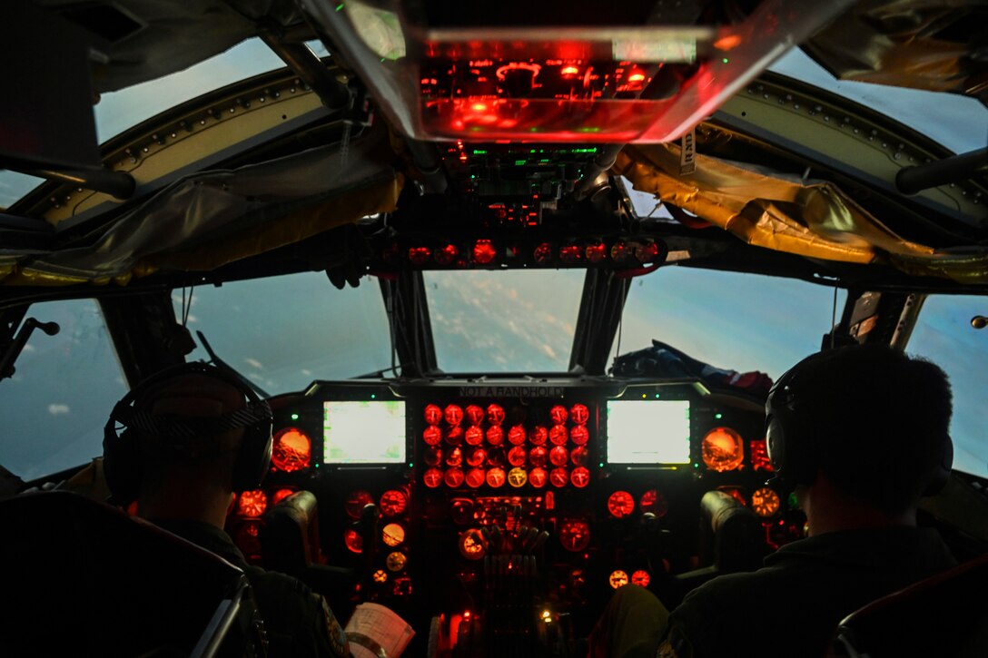 Two pilots sit in cockpit illuminated by red lights.