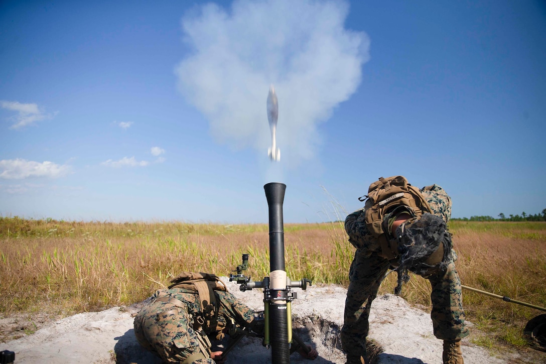 Two Marines crouch next to a mortar round that has fired.