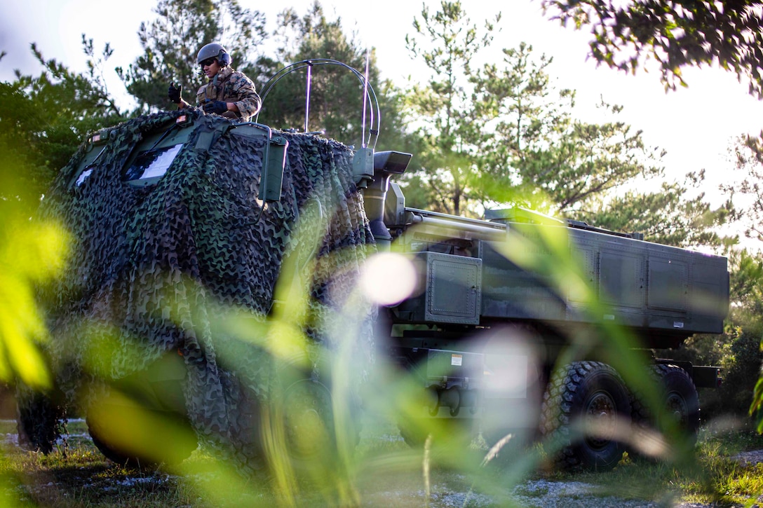 A Marine rides in a military vehicle through a wooded area.