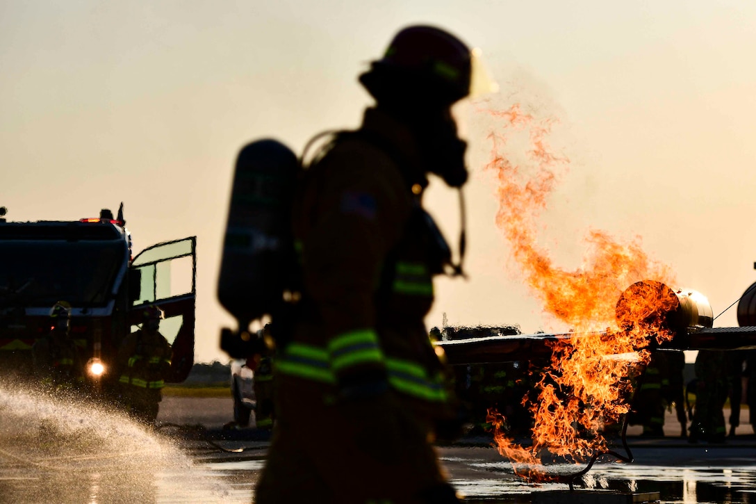 An Air Force firefighter walks in front of an aircraft fire.