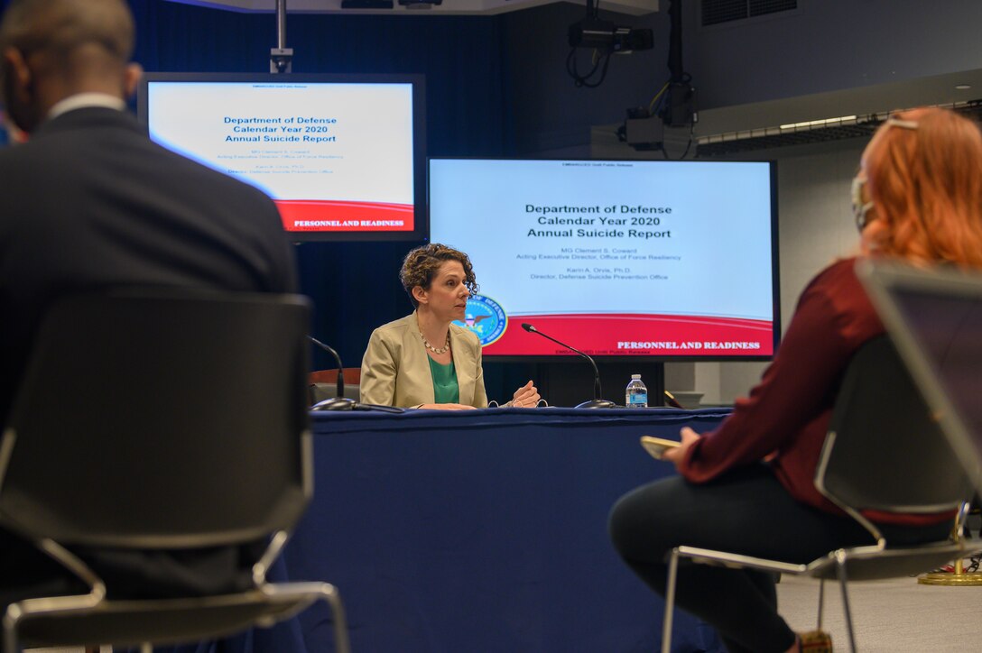 A woman sitting at a table speaks to a group of people.