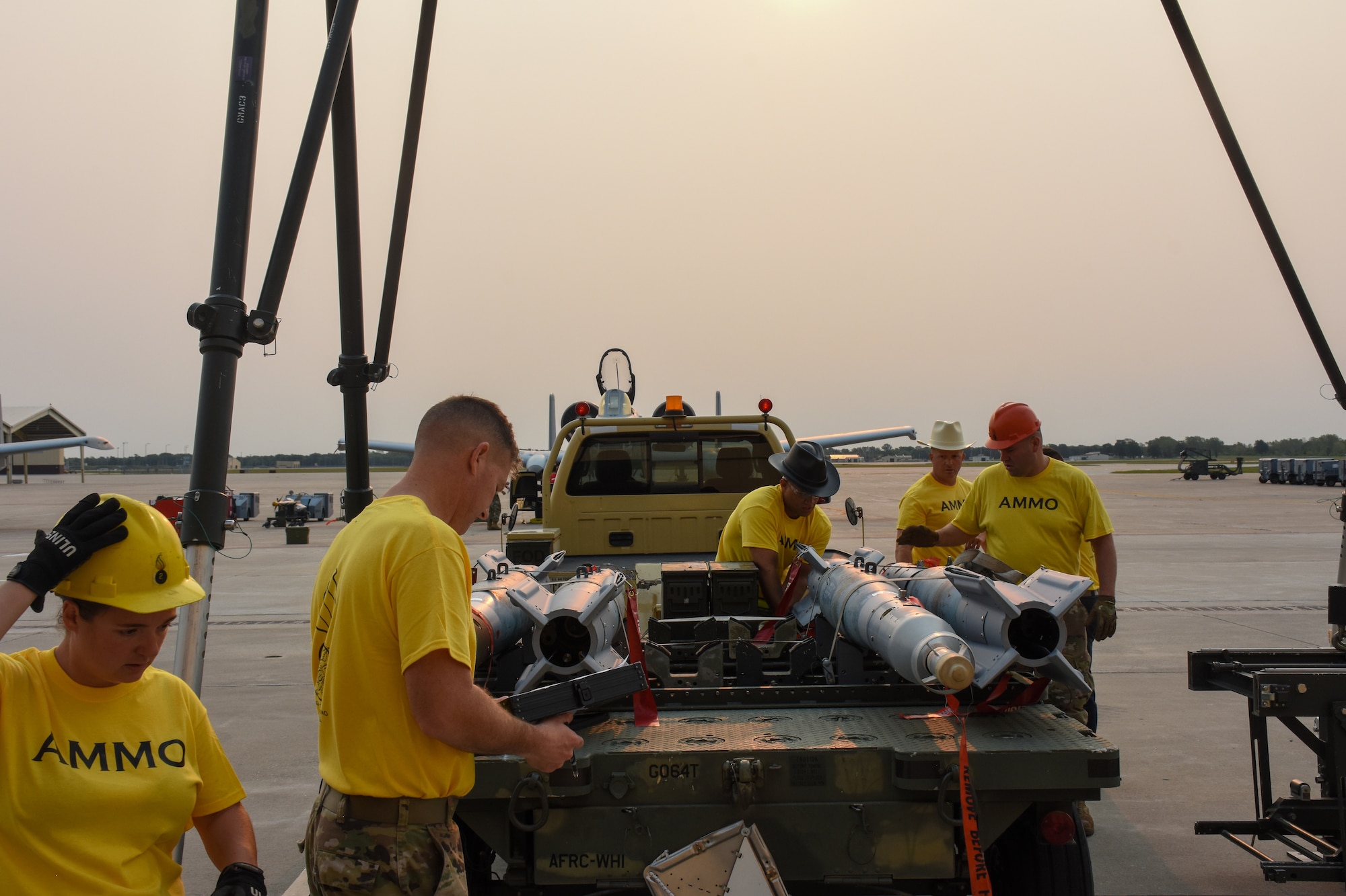 Five people in yellow shirts inspect a trailer with four bombs on it.