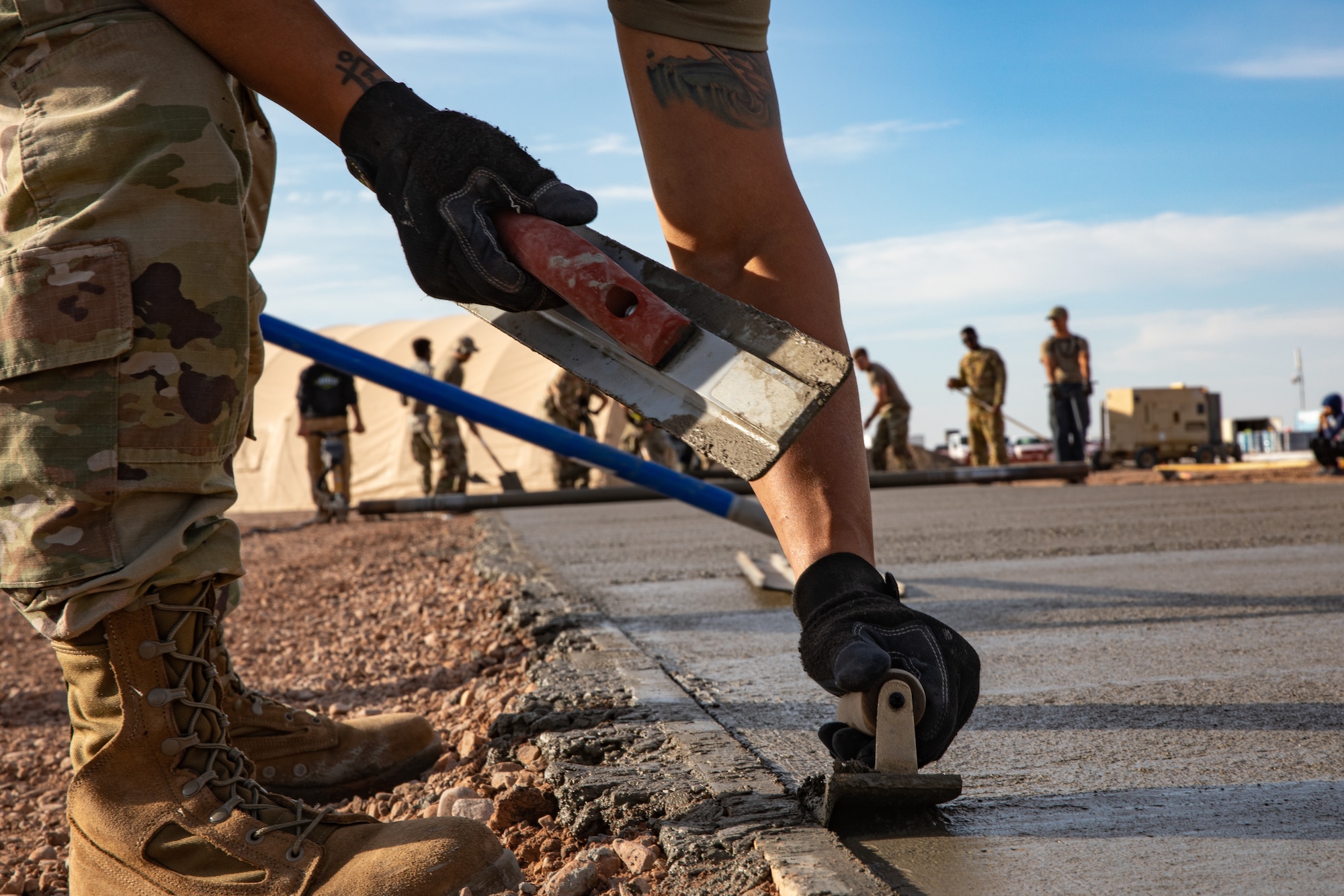 Airmen assigned to Task Force-Holloman smooth fresh concrete for a recreational area for Afghan evacuees on Holloman Air Force Base, New Mexico, Sept. 23, 2021. The Department of Defense, through the U.S. Northern Command, and in support of the Department of State and Department of Homeland Security, is providing transportation, temporary housing, medical screening, and general support for at least 50,000 Afghan evacuees at suitable facilities, in permanent or temporary structures, as quickly as possible. This initiative provides Afghan evacuees essential support at secure locations outside Afghanistan. (U.S. Army photo by Spc. Nicholas Goodman)