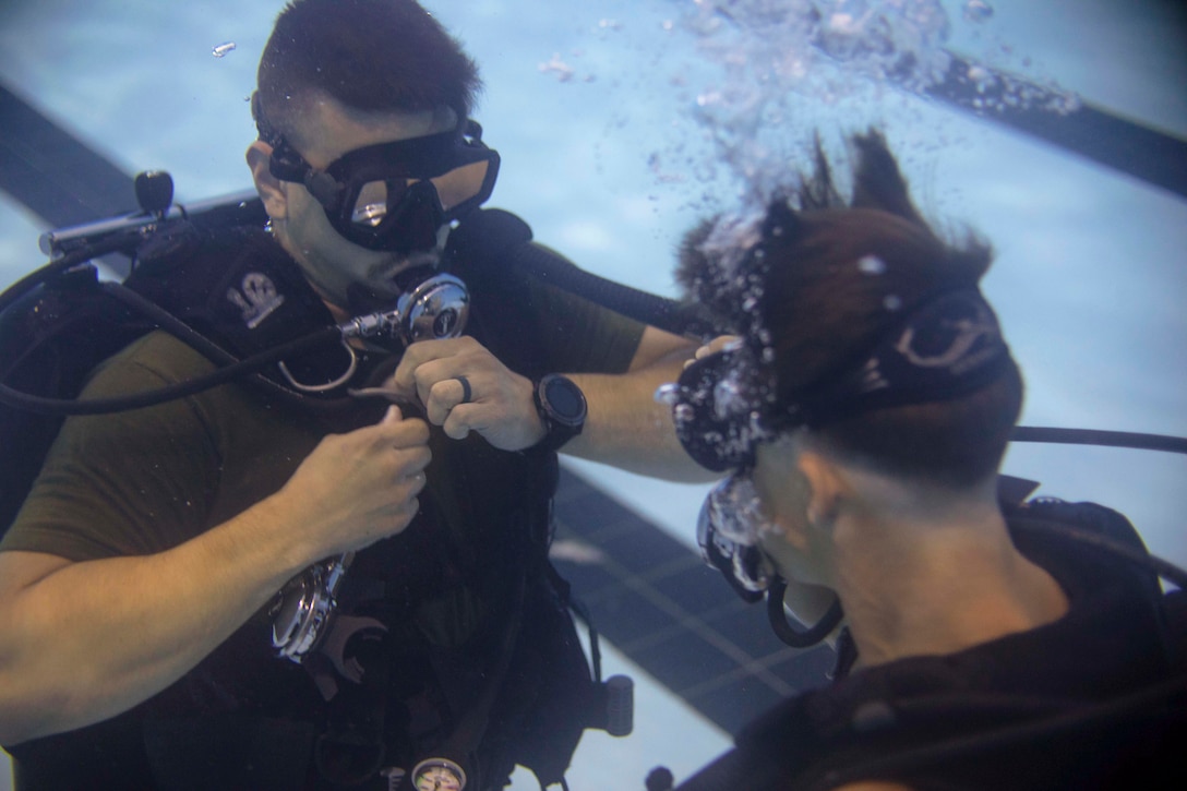 Two Marines wearing scuba diving gear practice breathing underwater.