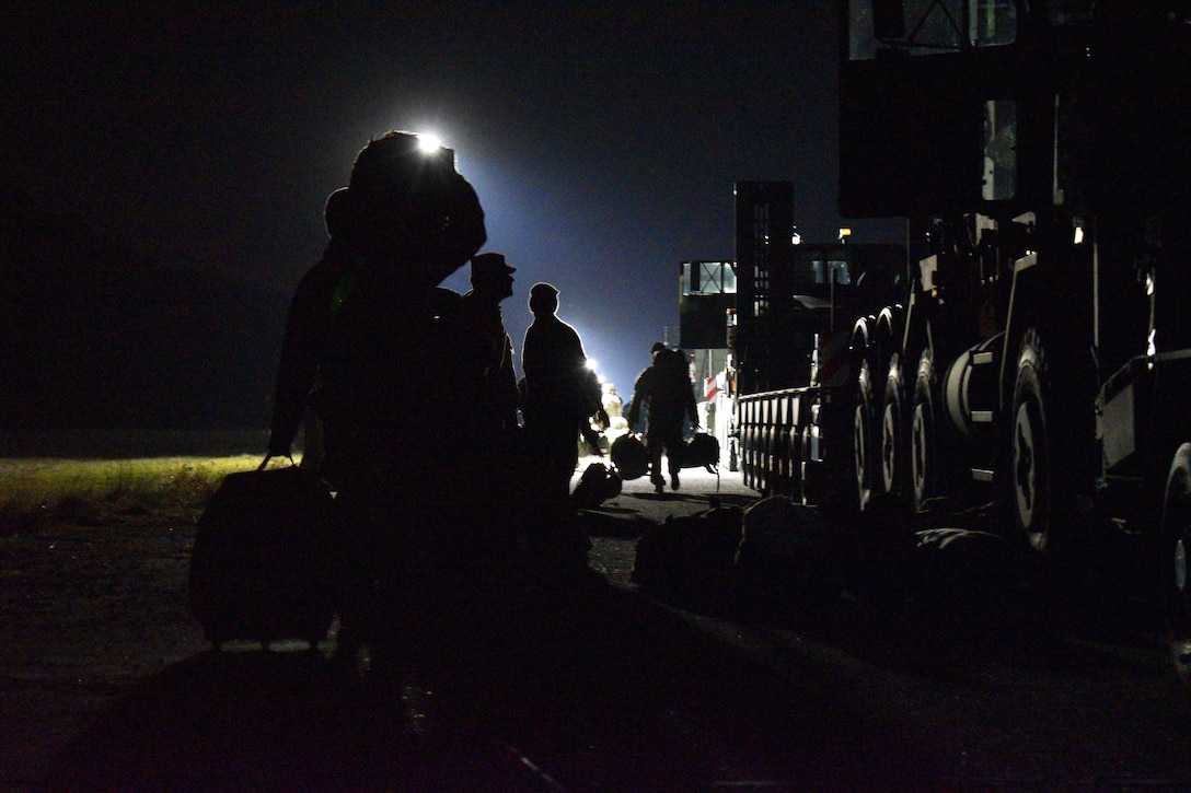 Soldiers take personal equipment to truck tractors at an airstrip.