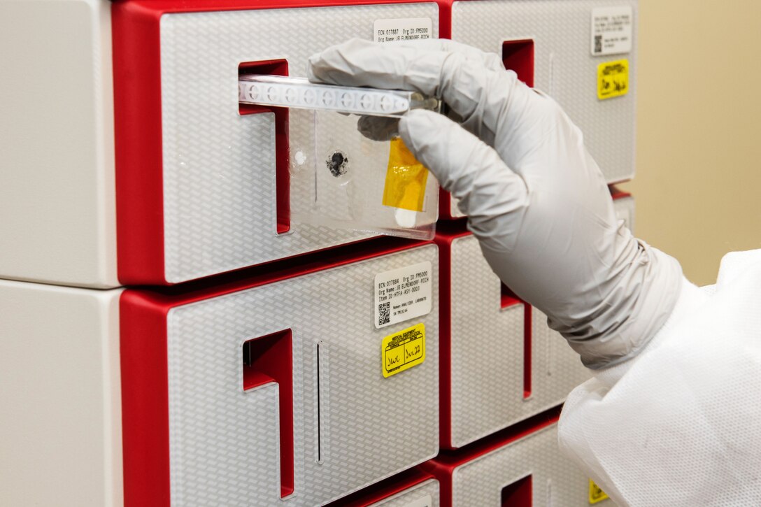 A person wearing personal protective equipment inserts a small container into a molecular analyzer to test for COVID-19.