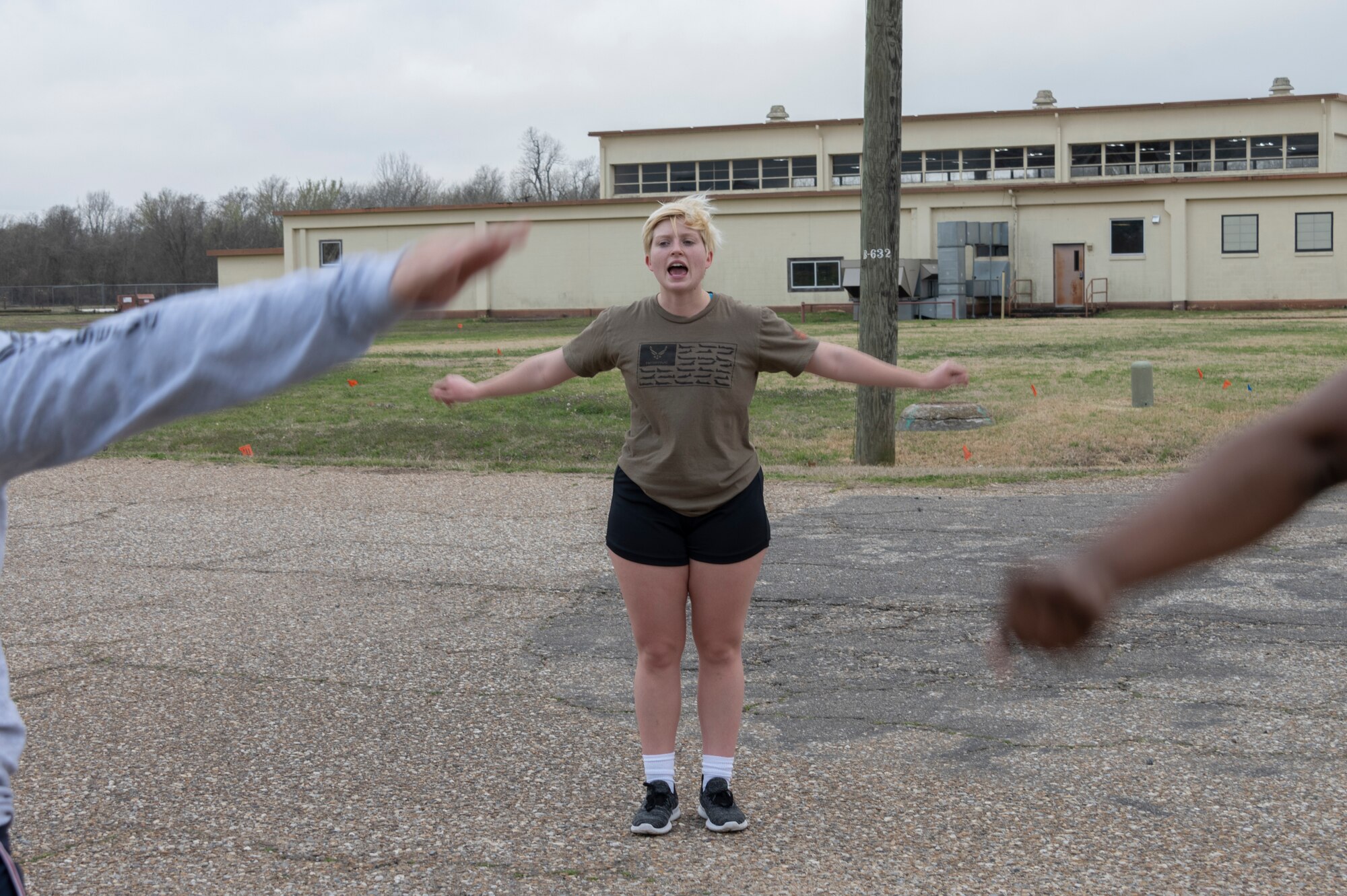woman stands outside doing arm rotation exercises.