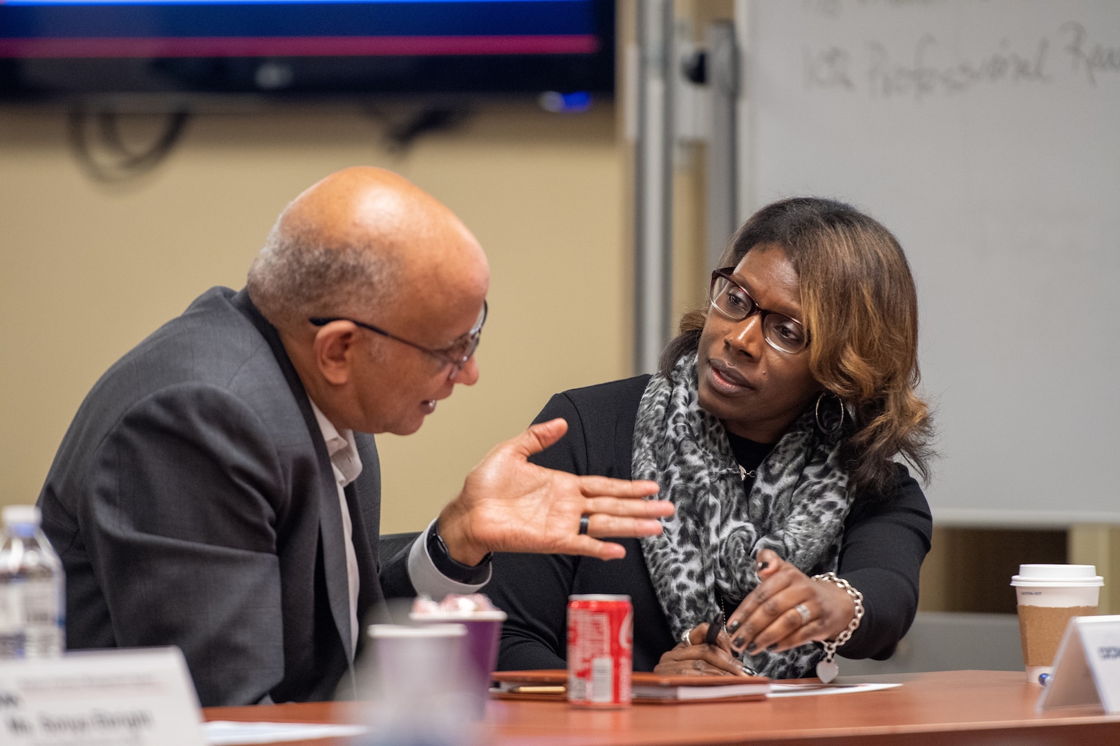 A man and a woman sitting at a table talk to one another.