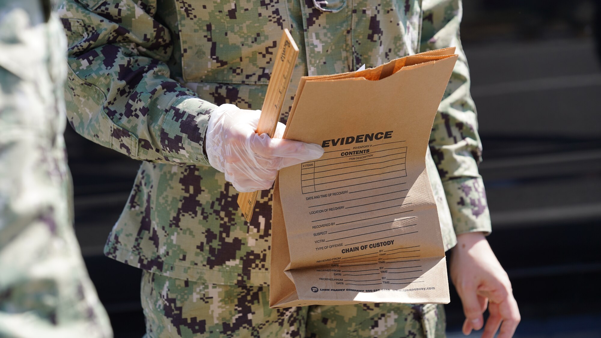 A U.S. Navy security forces member holds an evidence bag in a mock crime scene at Keesler Air Force Base, Mississippi, March 28, 2022. Participants gathered evidence and wrote statements that were used in a mock court martial the next day. (U.S. Air Force photo by Airman 1st Class Elizabeth Davis)