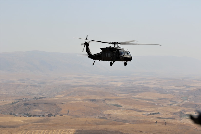 A helicopter flies over a desert landscape.