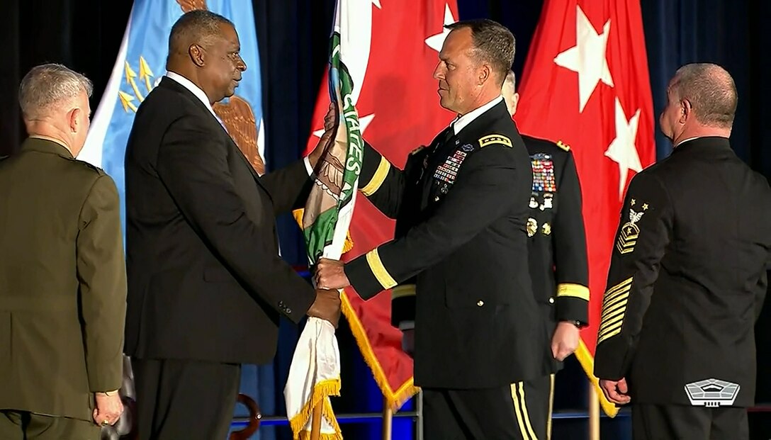 A man in a suit passes a flag to a man in a military uniform.