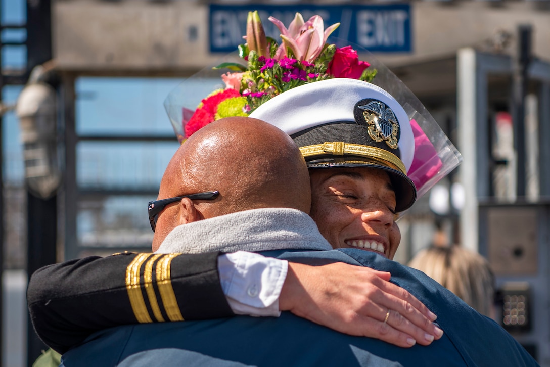 A sailor embraces a loved on holding flowers.