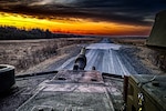 A military vehicle travels down a dirt road at twilight.