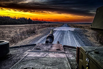 A military vehicle travels down a dirt road at twilight.
